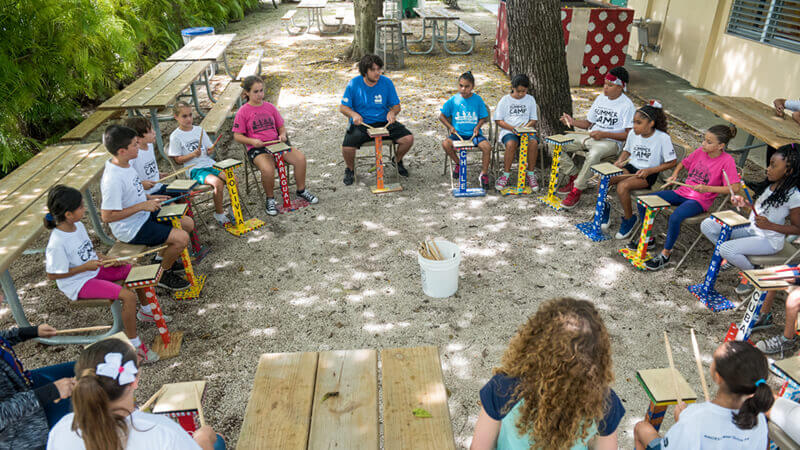 Campers sitting in a circle playing a wooden drum