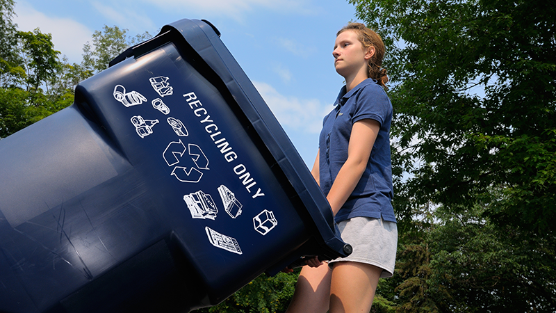 young girl rolling a recycling cart out