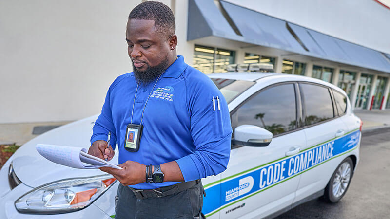 A Miami-Dade County code compliance officer standing outside of his work car.