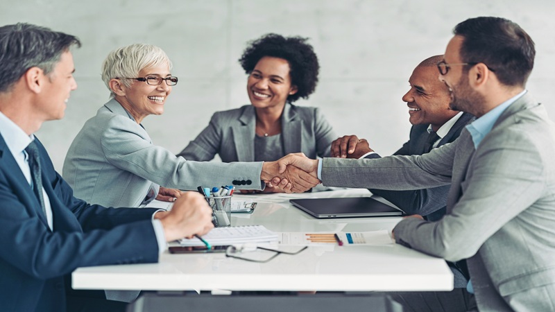 Businesswomen and men shaking hands at a table